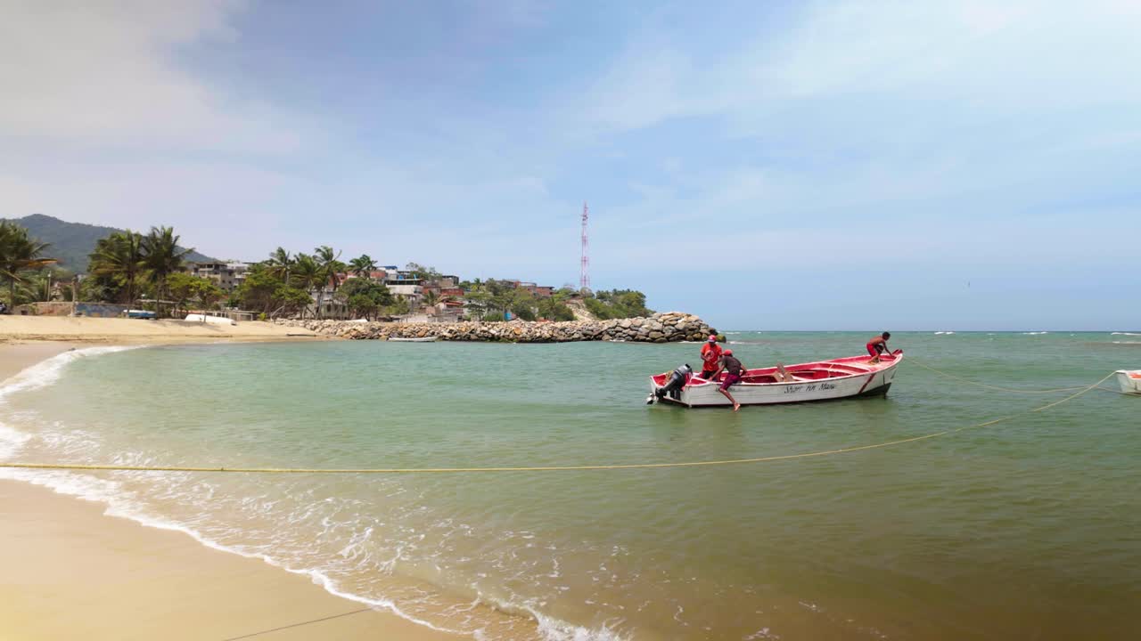 A child swims toward the beach as two fishermen wait near a small boat on turquoise water - Venezuela