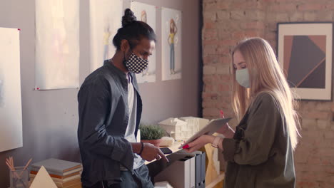 two multiethnic colleagues with face masks discussing a new project in an animation studio