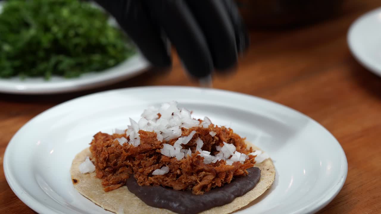 Putting chop onion and coriander cilantro on top of mexican taco with grill gloves