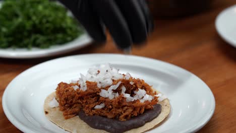 putting chop onion and coriander cilantro on top of mexican taco with grill gloves