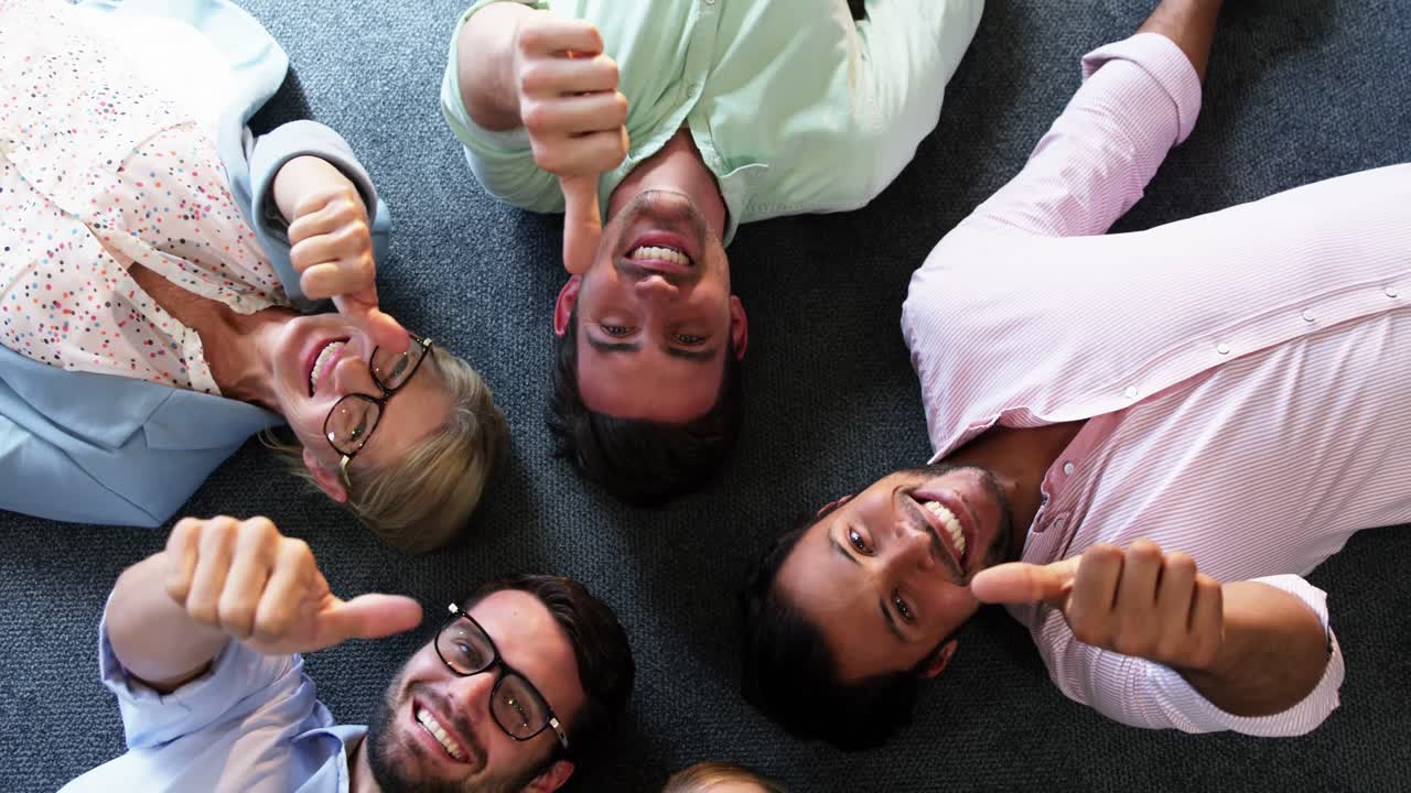 Portrait of businesspeople showing thumbs up while lying on the floor