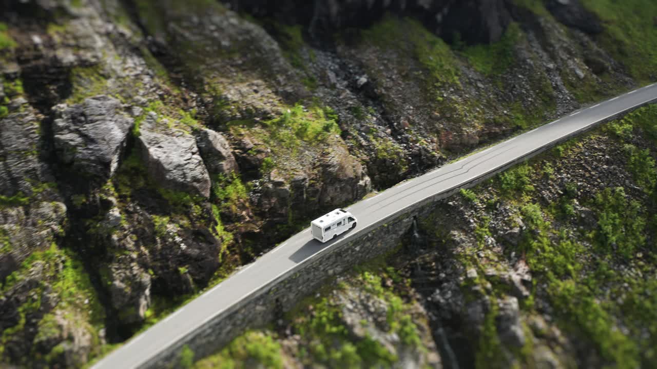 A motorhome climbs a winding Trollstigen road which follows the steep cliffs near a cascading waterfall, offering a breathtaking view. an aerial tilt-shift video.