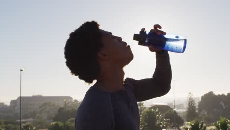 Fit-african-american-man-exercising-outdoors-in-city,-resting-and-drinking-from-water-bottle