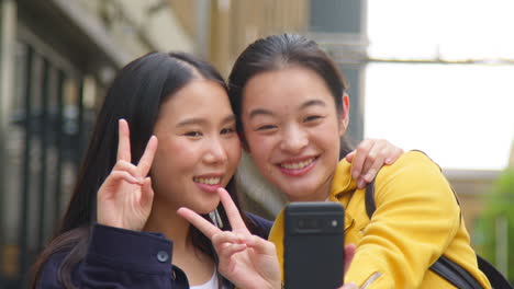 two smiling young female friends posing for selfie in urban setting together