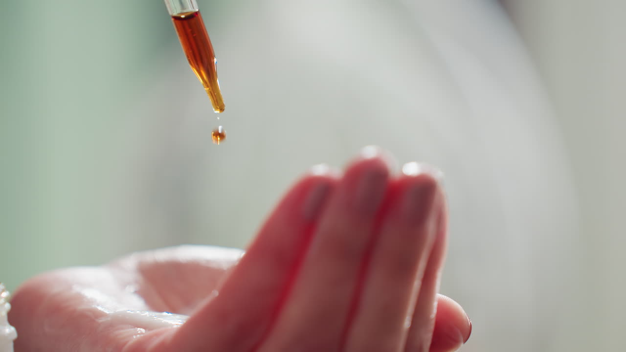 Mani con olio ambrato, primo piano di palmi che raccolgono il siero, intima scena di cura di sé con olio ambrato in ambiente rilassante, primo piano di mani che cullano un siero dorato luminoso in un ambiente spa tranquillo