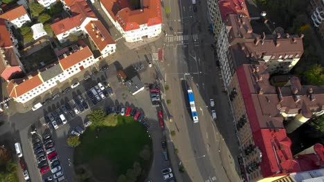 Aerial-of-city-road-with-moving-bus,-parked-cars-and-large-buildings