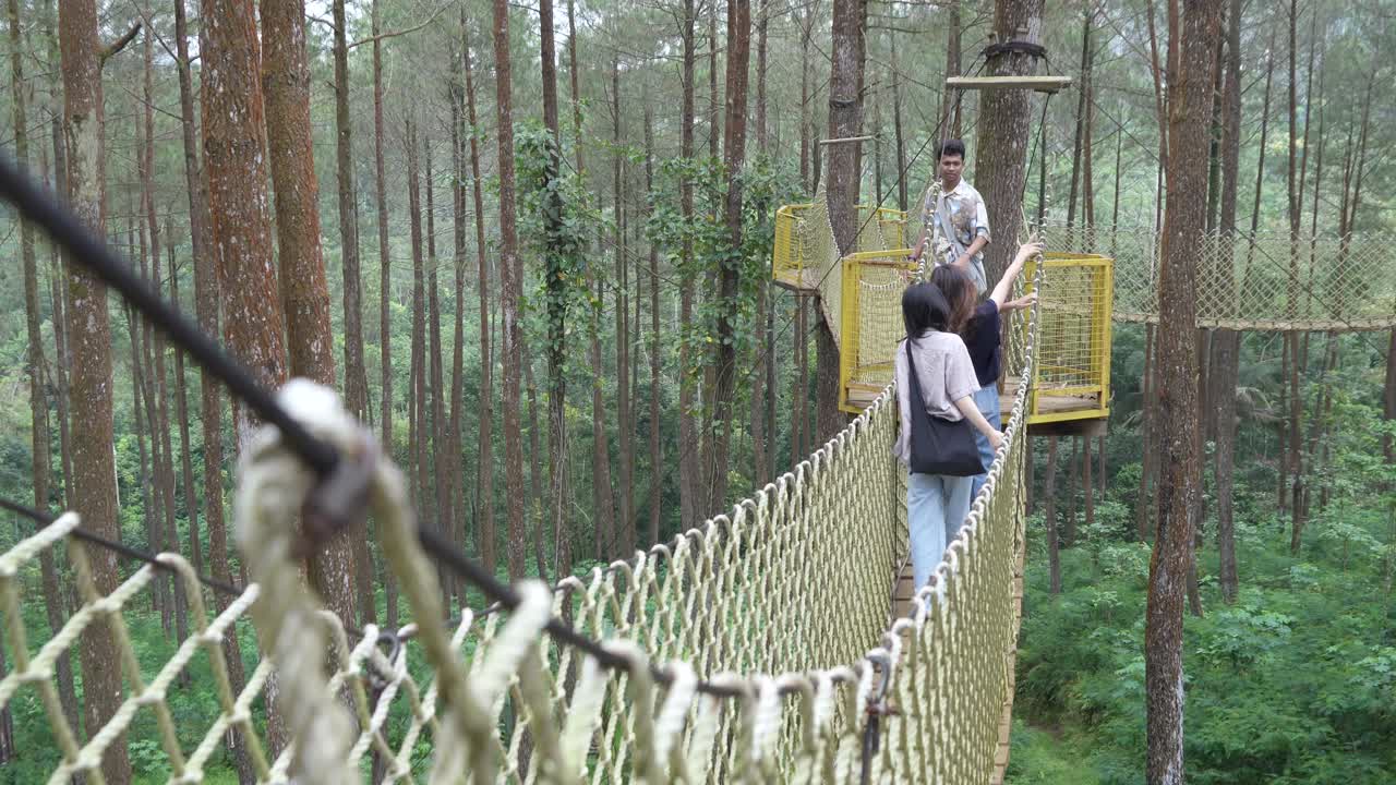 Young Asian Friends Crossing Rope Bridge in Forest Adventure