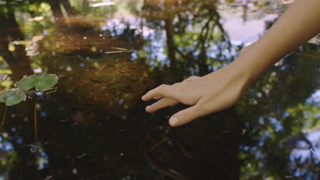 woman hand touching water in pond with finger making ripple