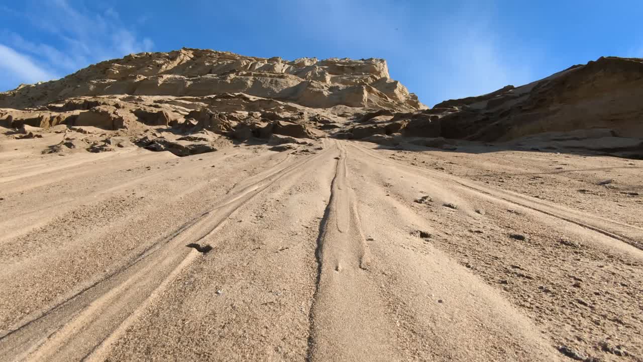 A vast sandy landscape with a large dune or cliff under a bright blue sky
