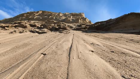 a vast sandy landscape with a large dune or cliff under a bright blue sky