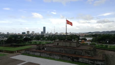 Aerial-shot-of-the-Vietnamese-flag-waving-in-the-wind-of-the-city-of-Hué,-Vietnam