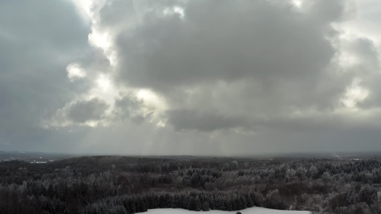 Aerial view of thick clouds over the forest landscape in countryside. Snow covered ground and sun rays through clouds in winter. Snow storm approaching.