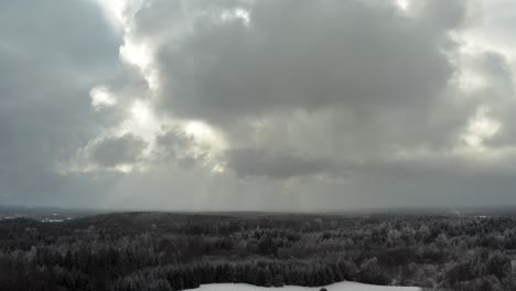 aerial view of thick clouds over the forest landscape in countryside. snow covered ground and sun rays through clouds in winter. snow storm approaching.