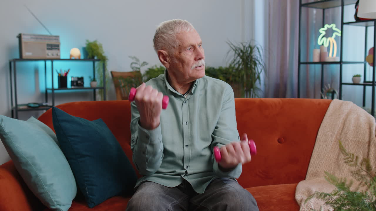 Mature grandfather man doing dumbbells weight lifting fitness exercises training strength at home