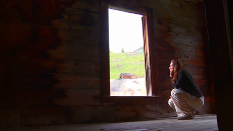 a woman sits in an abandoned house looking out the window