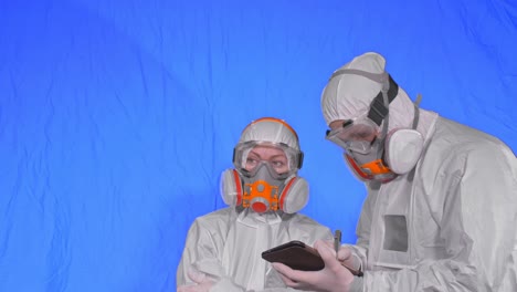 scientist virologist in respirator makes write in an tablet computer with stylus. man and woman wearing protective medical mask. chroma key blue.