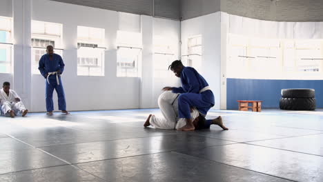 practicing judo, athletes grappling on mat while others watch in dojo