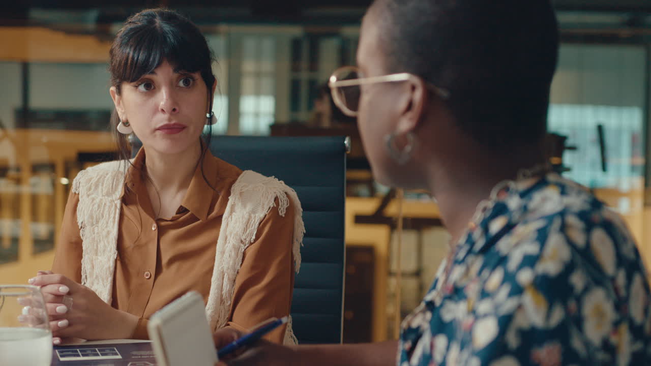 dos jóvenes compañeras de trabajo discutiendo en una reunión de oficina