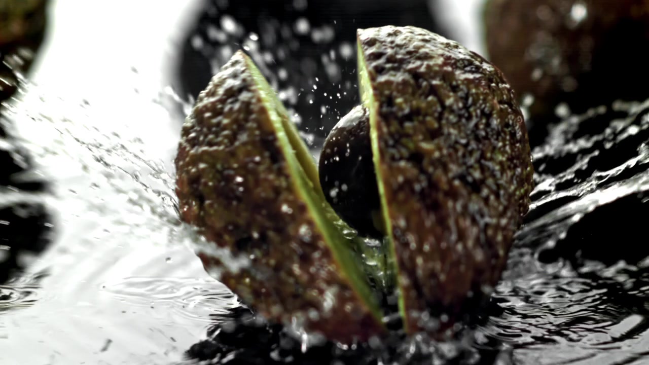 Avocado, die in Zeitlupe ins Wasser fällt und sich halbiert