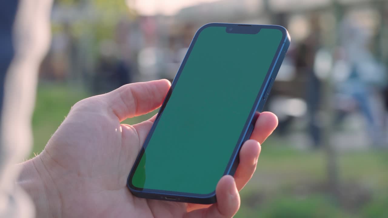 primer plano de 4k de la mano del hombre sosteniendo un teléfono inteligente con pantalla de maqueta verde llave croma al aire libre