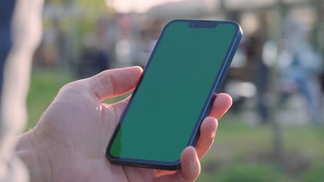 primer plano de 4k de la mano del hombre sosteniendo un teléfono inteligente con pantalla de maqueta verde llave croma al aire libre