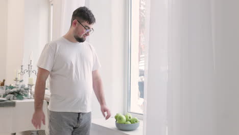 boy picking an apple from a fruit bowl near the window