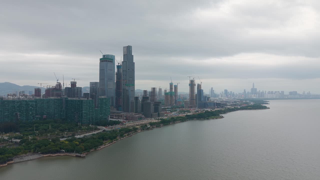 Wide drone shot of Shenzhen Bay Park showing modern skyscrapers, ongoing construction, coastal landscape, and urban development around the China Merchants Bank complex