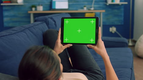 Over-the-shoulder-view-of-casual-woman-sitting-on-sofa-using-tablet-computer