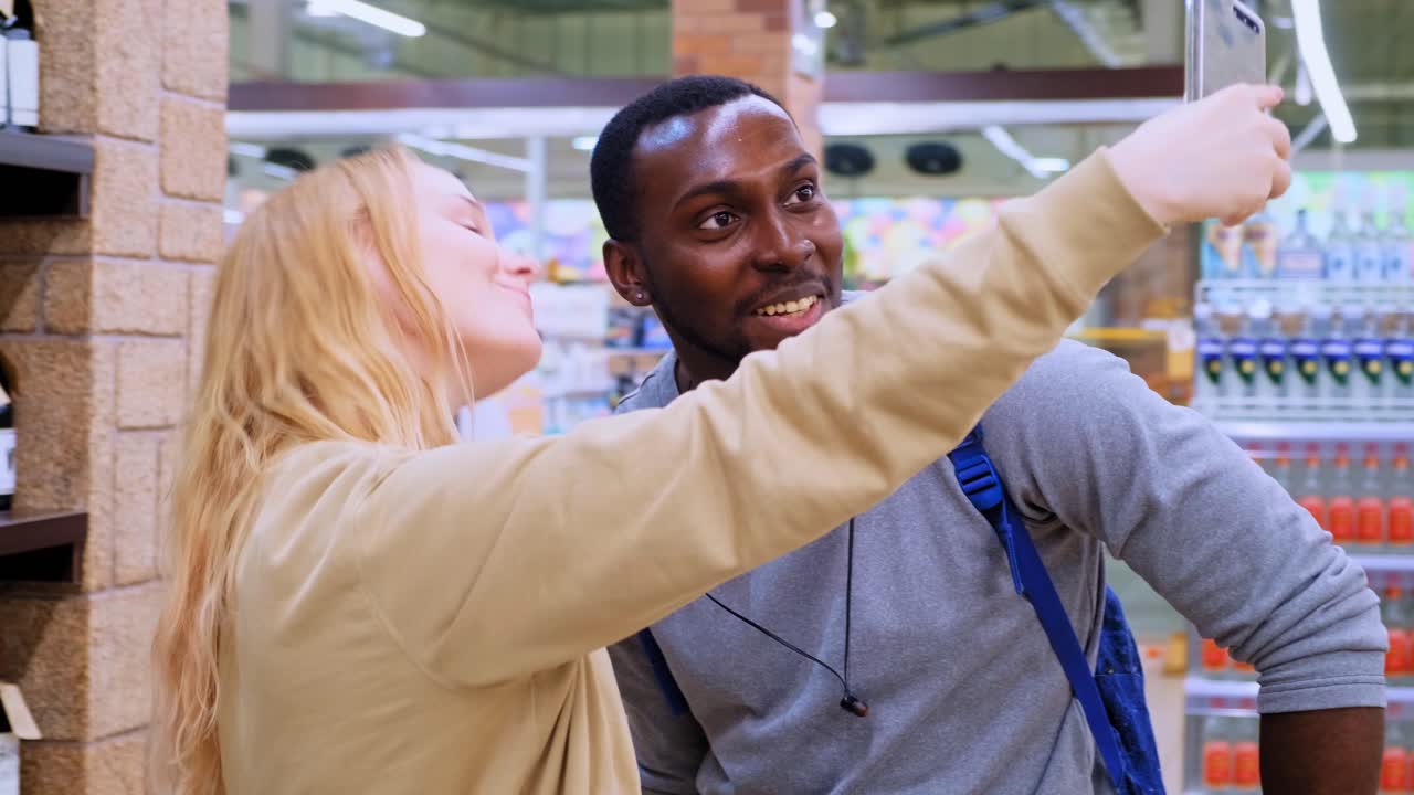 Capturing Moments Together: A Cheerful Couple Smiling as They Take a Selfie in a Brightly Lit Grocery Store Full of Colorful Snacks and Fresh Products