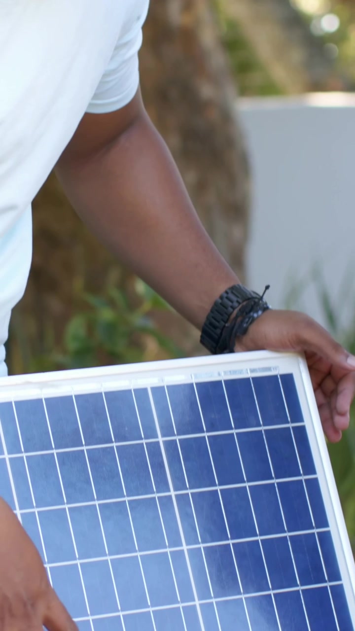 Video verticale: Un giovane con una maglietta blu si gira e guarda un adulto arrivare con un pannello solare nel patio, imparando.