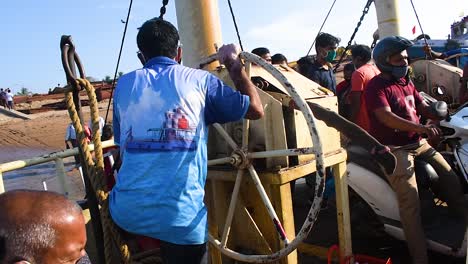 a worker in ferryboat rotating a big wheel of a winch of the boat and trying, an indian worker or sailor closing the winch of the boat with a big wheel in boat full of passengers and travelers