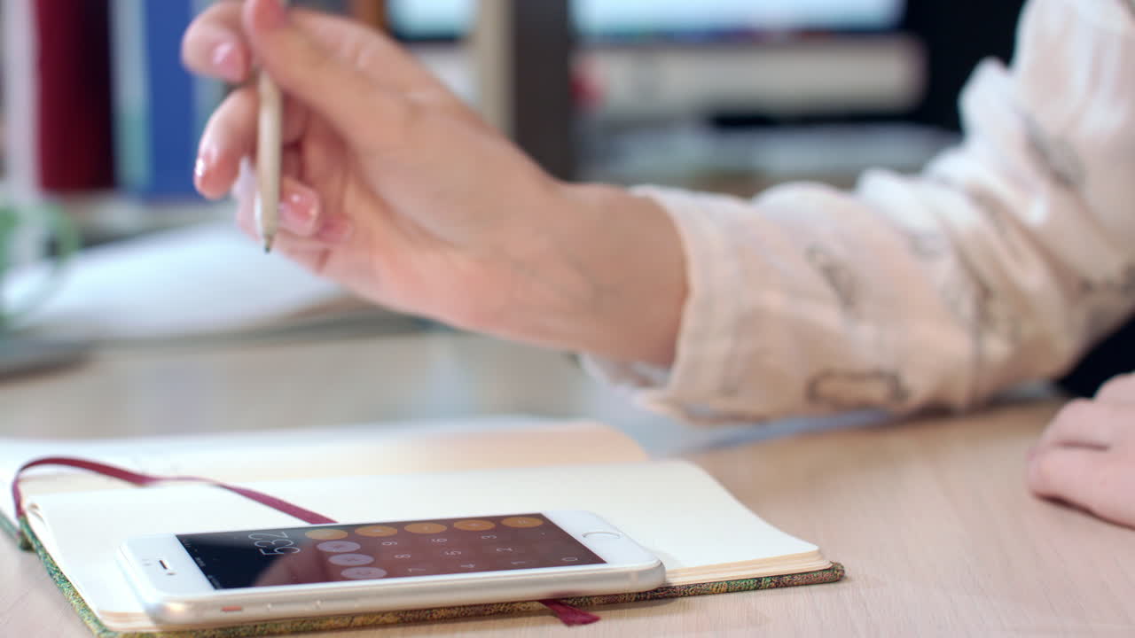 mano femenina usando teléfono móvil para calcular la ganancia en el lugar de trabajo de la oficina