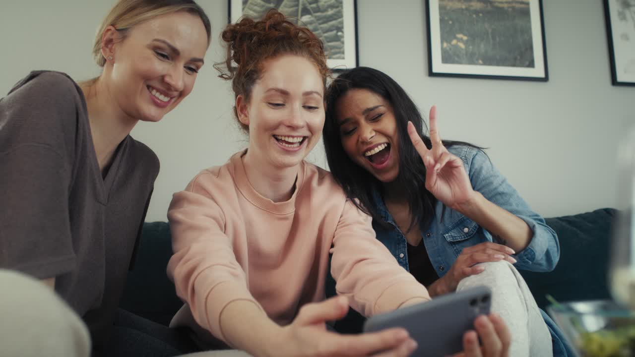 tres mejores amigos caucásicos divirtiéndose mientras se toman selfies en el sofá.