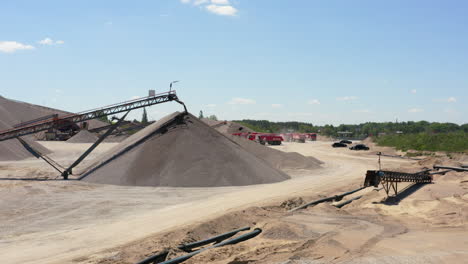 sand quarry with conveyor belts stacking material into large piles. industrial trucks and machinery in background. wide shot