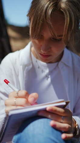 Young Woman Writing in a Notebook Outdoors