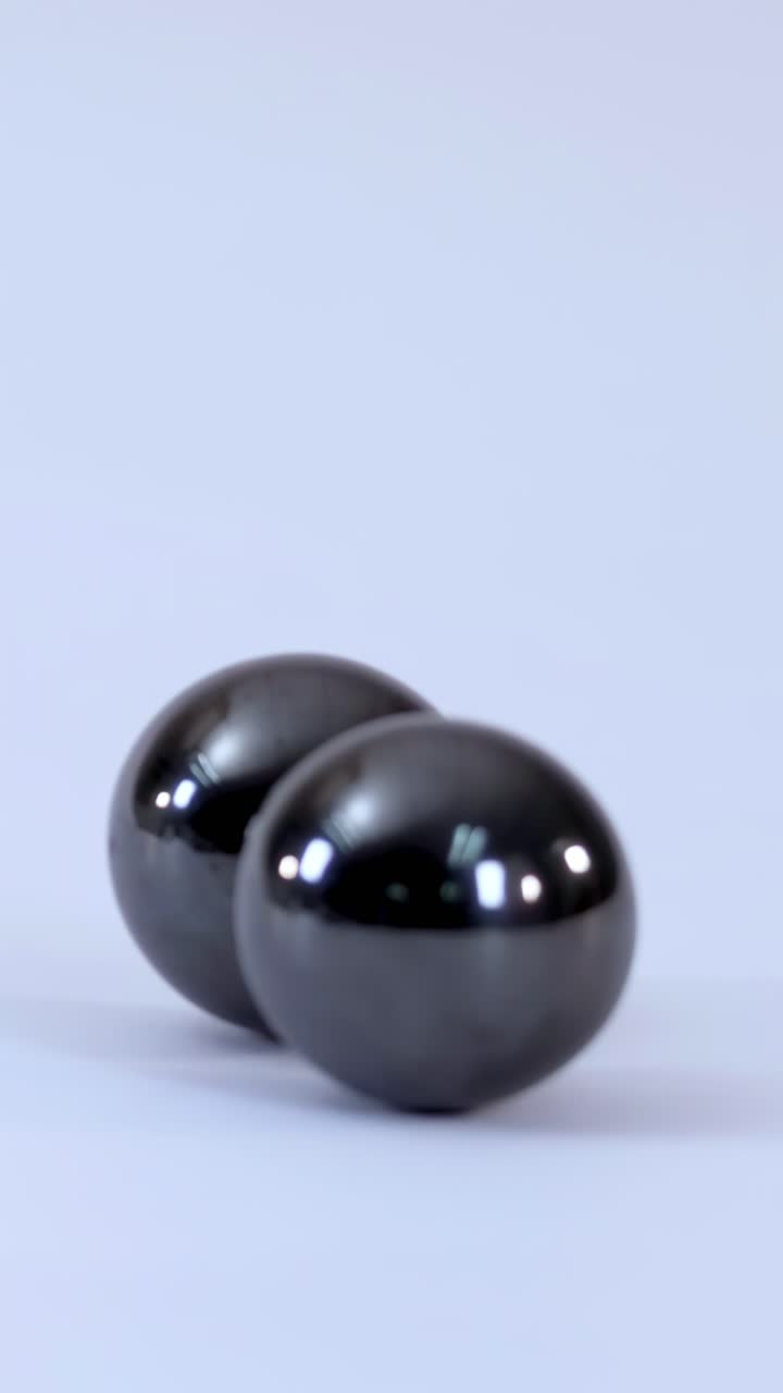 Close-up shot of metallic magnetic balls rolling and snapping together on a white background