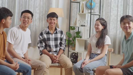 아시안 십대 그룹은 의자에 앉아서 집에서 토론하는 원을 형성하면서 카메라에 미소 짓고 있습니다.