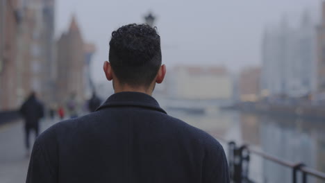 man walking along a city river on an overcast day