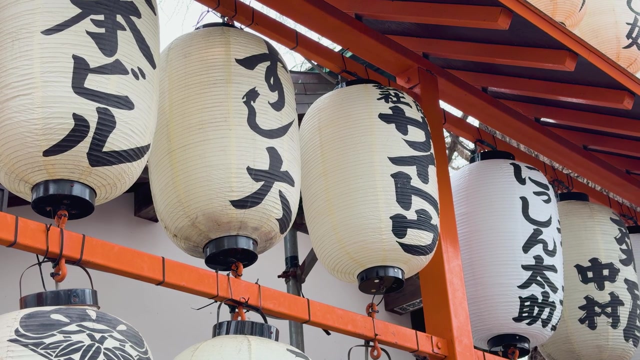 Lanterne di carta bianche tradizionali con calligrafia nera appese a cornici di legno arancioni a Tokyo.