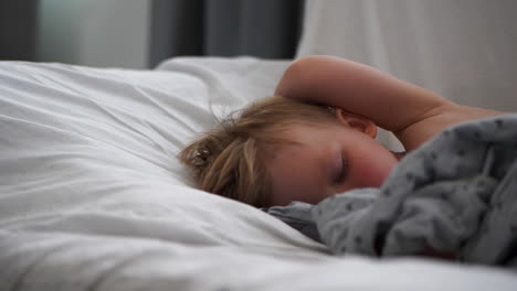 close pan shot of young blonde boy with rosy cheeks sleeping in bed
