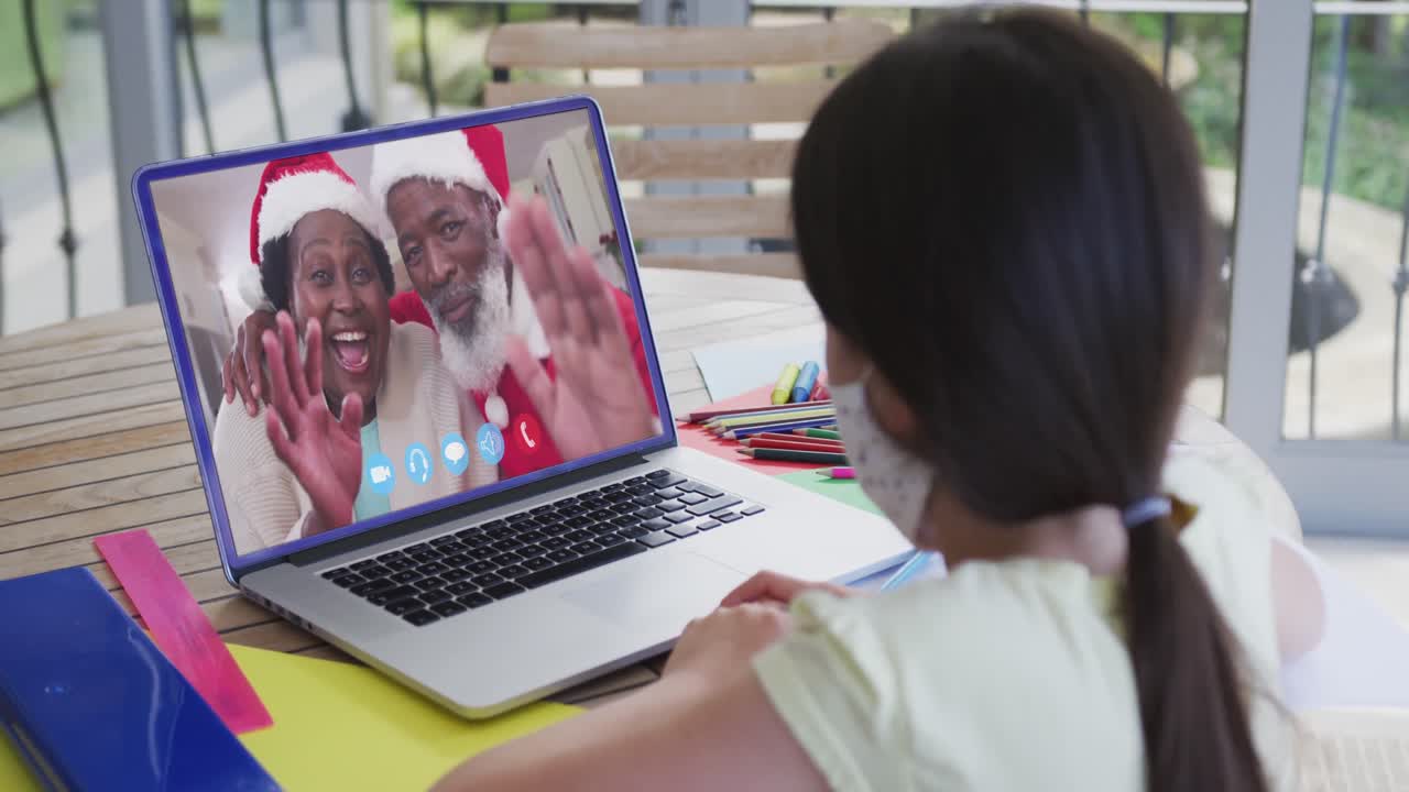 chica caucásica con máscara facial en la computadora portátil video chat durante la navidad en casa