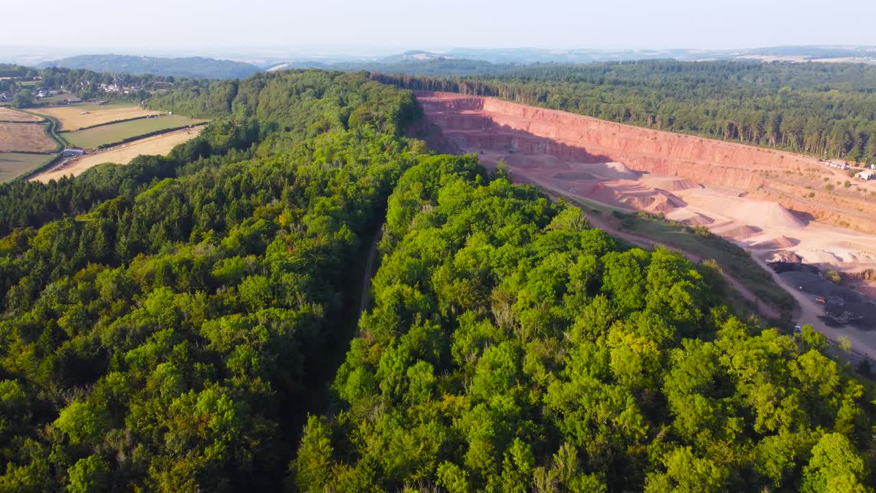 Retreating Aerial Showing Deep Quarry Extracting Stone Sand Gravel Surrounded by Dense Forest and Fields. Heavy Mining Excavating Industry Surrounded by Natural Environment