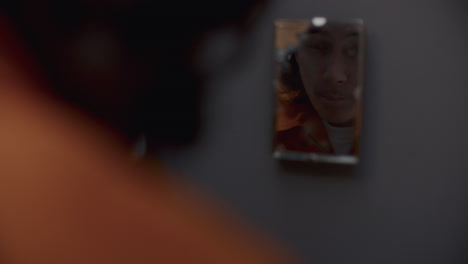 inmate washing face and looking in mirror on wall in prison cell