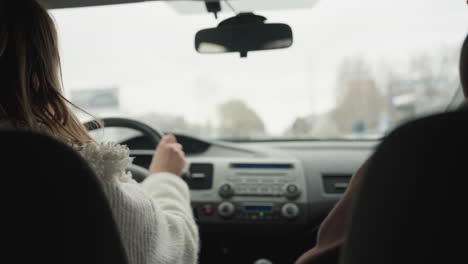 behind view of people on road trip driving through snowy urban highway with blur surroundings and passing car seen through car window during journey with blurred signs and buildings
