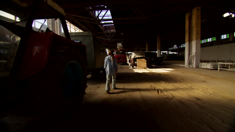 person walking in an empty warehouse with old trucks
