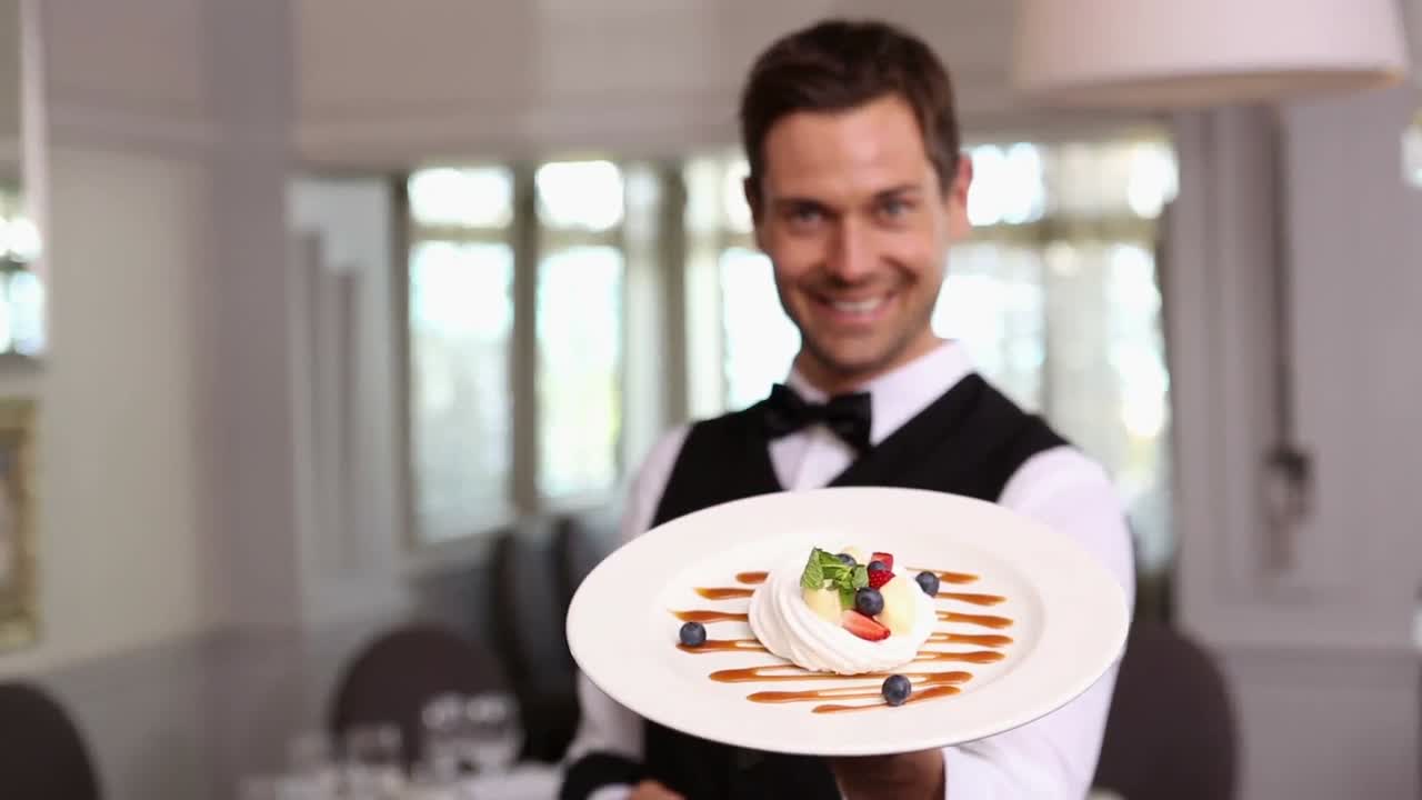 un guapo camarero que muestra un plato de postre