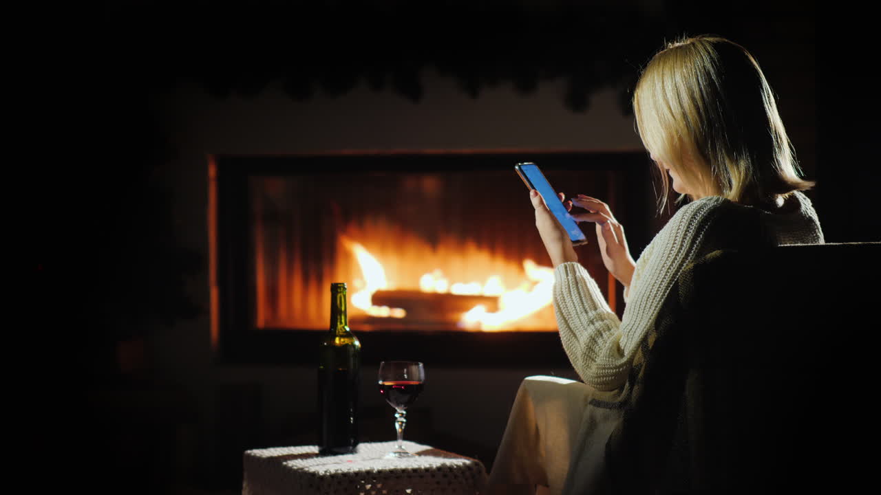 agradable velada junto a la chimenea una mujer usa un teléfono inteligente cerca de una copa de vino