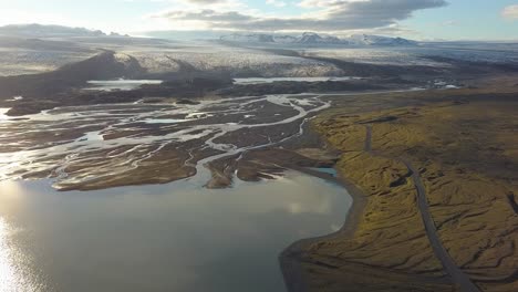 carretilla aérea fuera de los fiordos y el lago en las tierras bajas, glaciar breiðamerkurjökull en el fondo en una hora dorada nublada, parque nacional vatnajökull, islandia