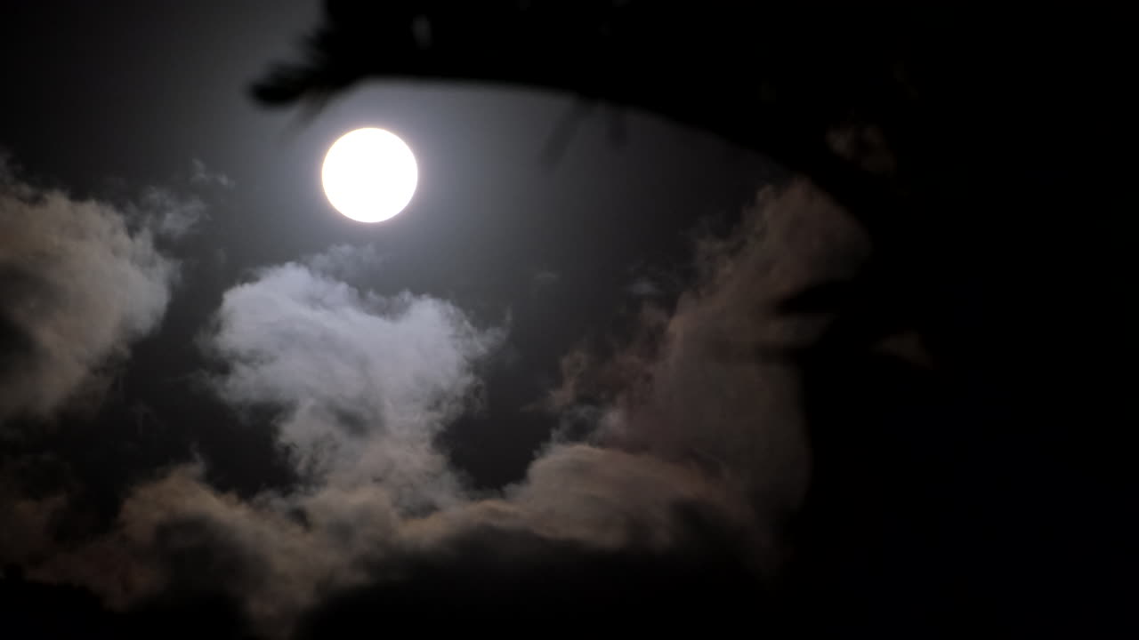 Round illuminated orb of full moon in night sky with passing clouds
