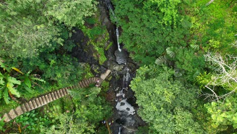 group of people enjoy gembleng waterfall, bathing natural pools in sidemen village jungle rainforest - aerial top down